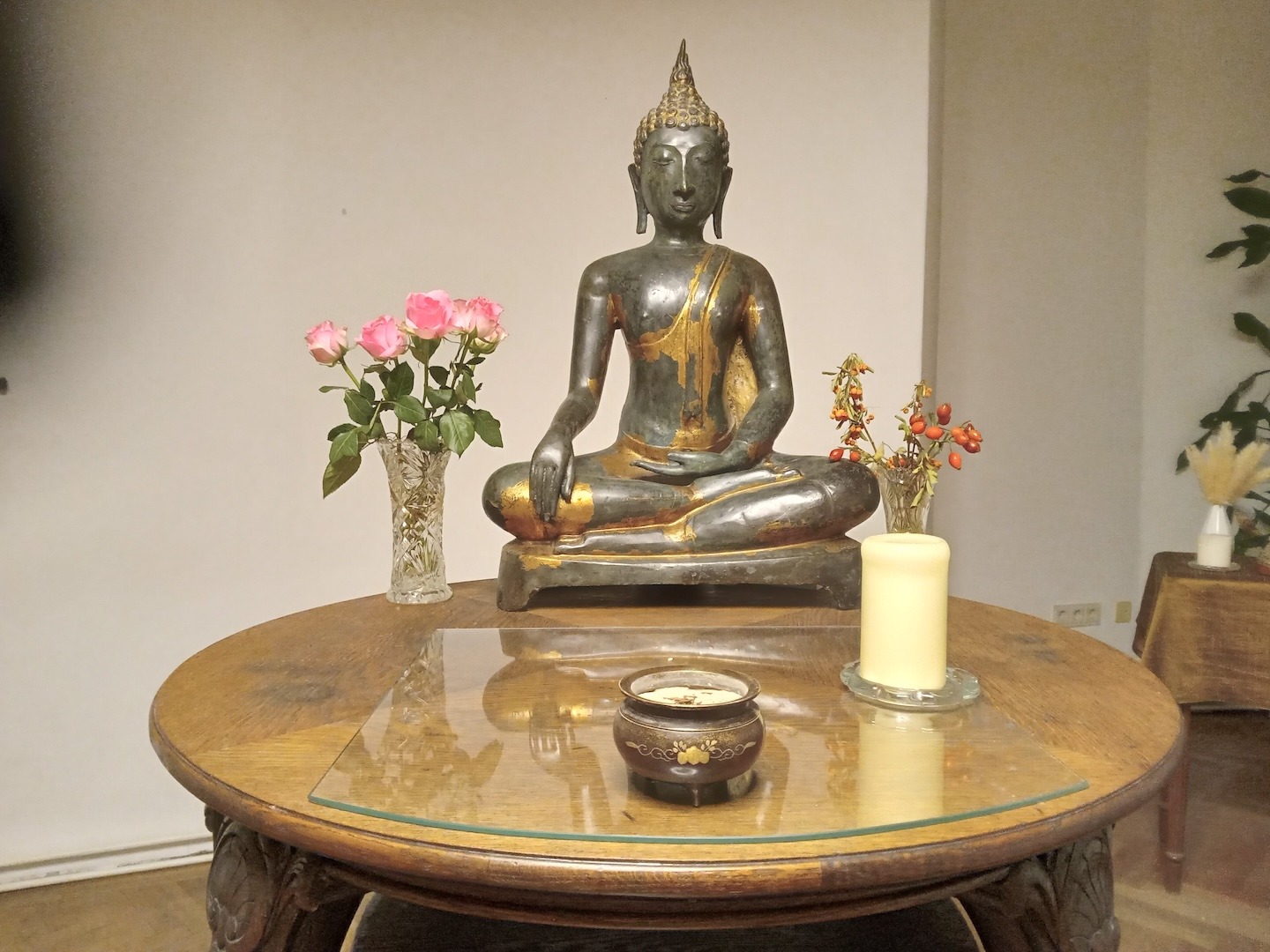 Kleiner Altar mit Kerze, Blumen, Räucherschale und einer Buddha Statue in der klassischen Erdberührungsgeste.
